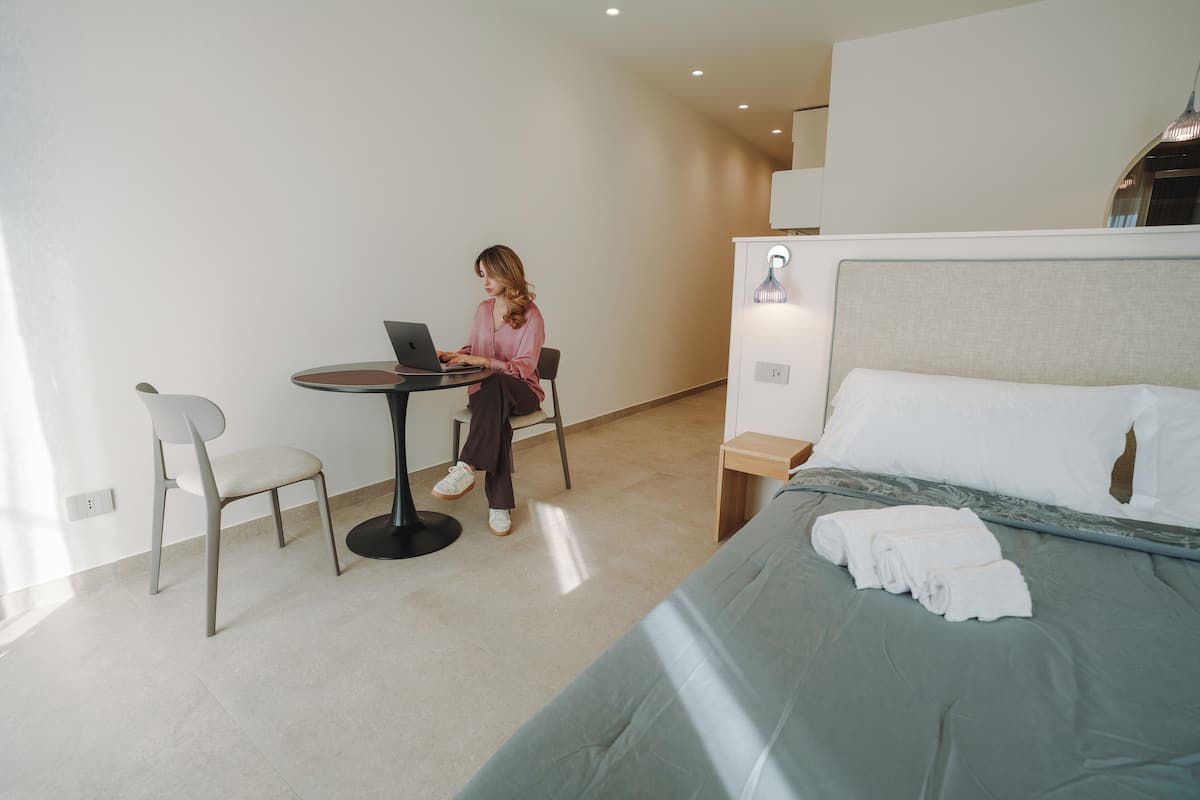 A hotel room with a bed, a desk with a laptop, a chair, and a small table.