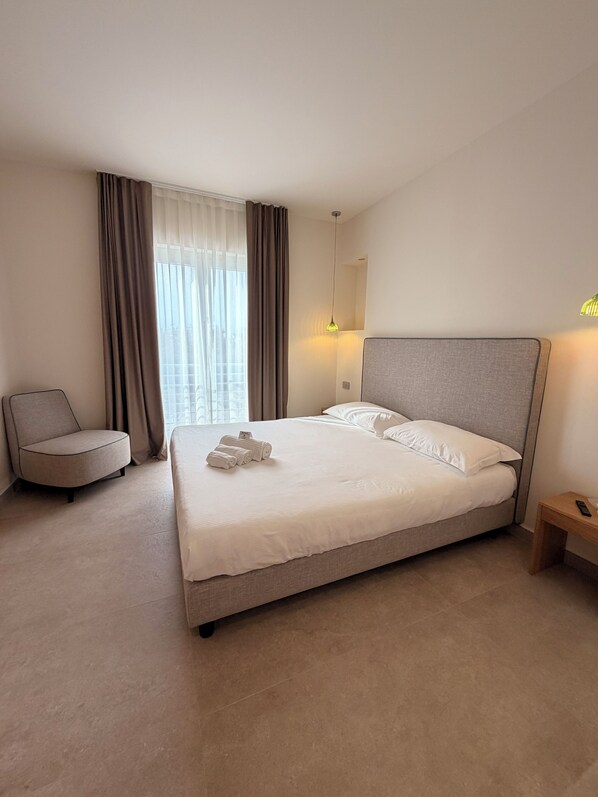Une chambre d’hôtel bien aménagée, avec un grand lit, une chaise, une table de chevet et une fenêtre avec des rideaux.