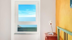 Een kamer met een raam dat uitkijkt op water, een tafeltje met een lamp en een groene balustrade.