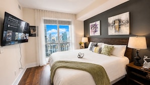 Ein modernes Hotelzimmer mit einem großen Bett, Blick auf die Stadt, Kunstwerken an der Wand und einem Flachbildfernseher.