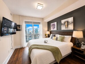Une chambre d’hôtel moderne dotée d’un grand lit, offrant une vue sur la ville, agrémentée d’œuvres d’art au mur et d’un téléviseur à écran plat.