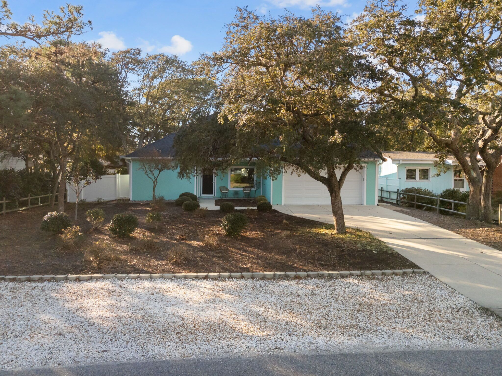 A single-story house with a garage, surrounded by trees and a gravel driveway.