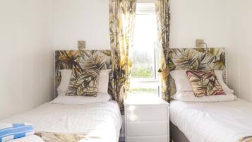 A double room with two beds, each with a headboard, a bedside table, and a window with curtains.