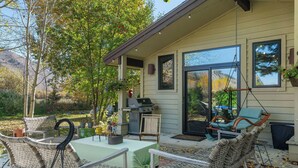 An outdoor patio with wicker furniture, a grill, and hanging chairs. - Luxury Teton Ski Getaway: Beautiful 4BR Home (Jackson)