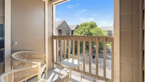 A balcony with wicker chairs and a small table, overlooking a residential area with houses and trees. - Landing Apartments San Antonio near Baptist Neighborhood Hospital (San Antonio)
