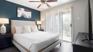 A hotel room with a bed, two bedside lamps, a ceiling fan, a window with blinds, and a TV on a stand. - Landing Apartments San Antonio near Baptist Neighborhood Hospital (San Antonio)