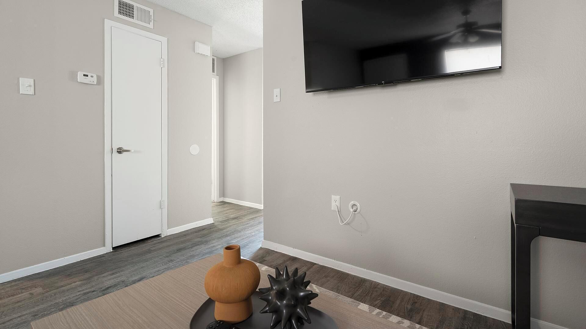 A modern living room with a flat-screen TV mounted on the wall, a door, and a small table with decorative items.