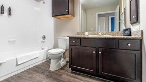Een badkamer met een badkuip, toilet, donkere houten kastjes en een granieten aanrecht.