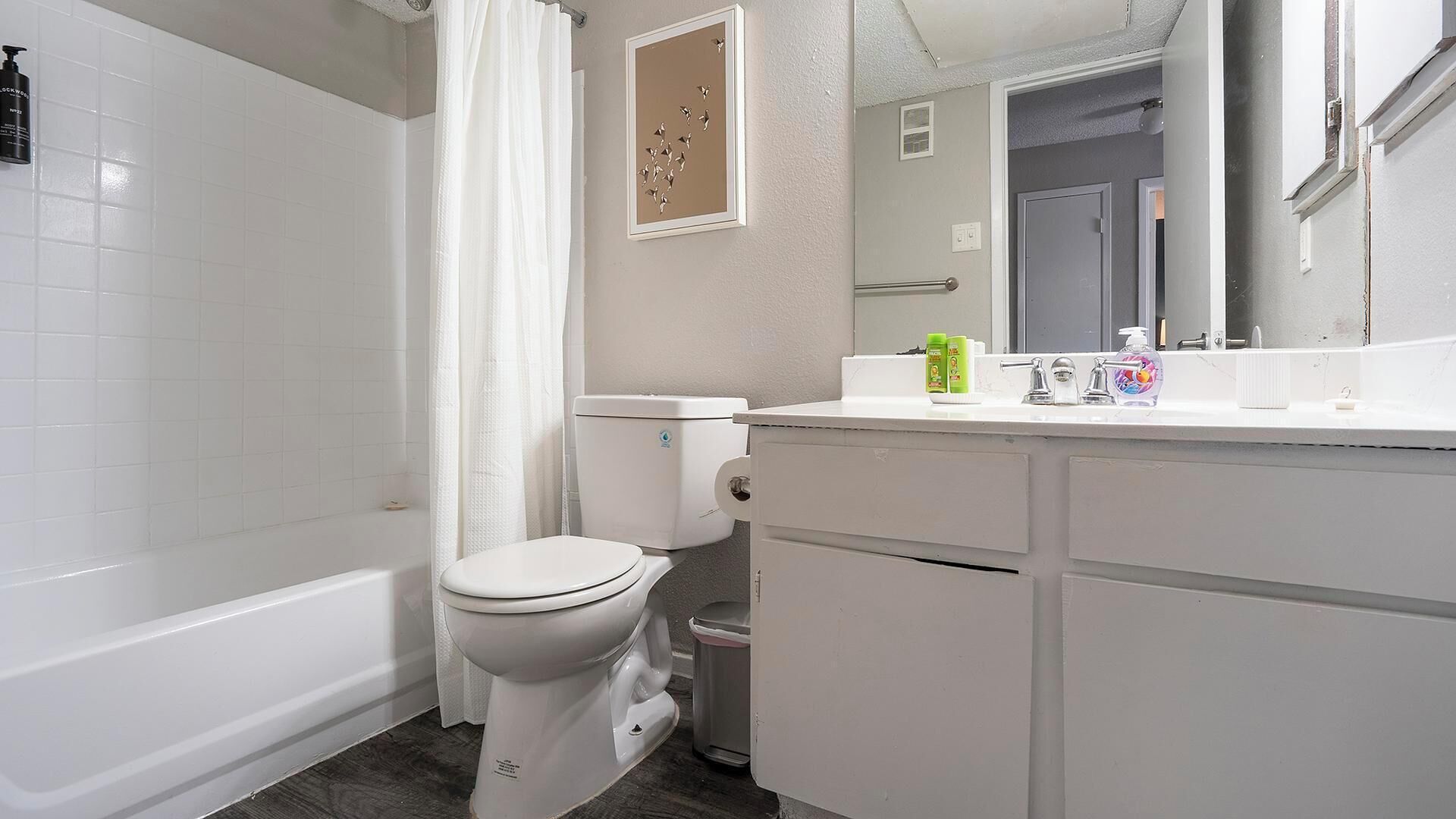 Een badkamer met toilet, douchegordijn, wastafel en verzorgingsproducten, en een spiegel.
