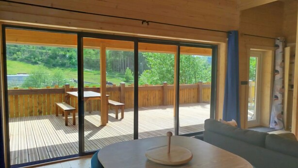 Un interior moderno con una terraza de madera, una zona de comedor y un amplio ventanal corredera que da a un espacio exterior.