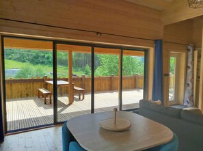 A modern interior with a wooden deck, a dining area, and a large sliding glass door leading to an outdoor space. - Chalet le ressourcé (Bussang)