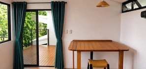 Een kamer met een houten tafel en een stoel, een raam met gordijnen en uitzicht op groen.