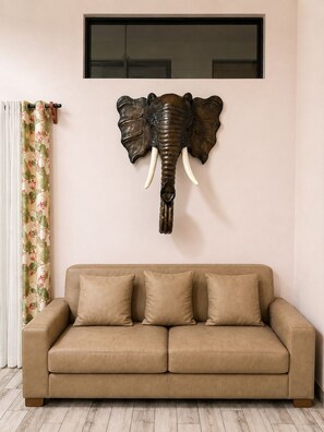 A room with a beige sofa, a wall-mounted elephant head sculpture, and a window with blinds. - Private Jungle Sanctuary • Ocean Sunset Views • Private Pool • Wildlife (Ojochal)