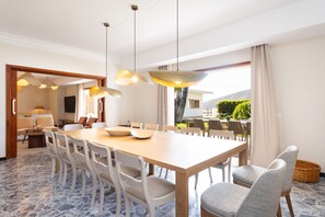 A dining area with a large wooden table, white chairs, and pendant lighting.