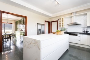 A modern kitchen with a large island, white cabinetry, and a stainless steel refrigerator.