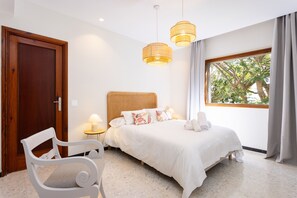 A bedroom with a bed, bedside table, lamp, and a view of trees through a window.
