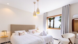 Ett hotellrum med två sängar, en sittgrupp med en fåtölj, ett fönster med utsikt och en spegel.