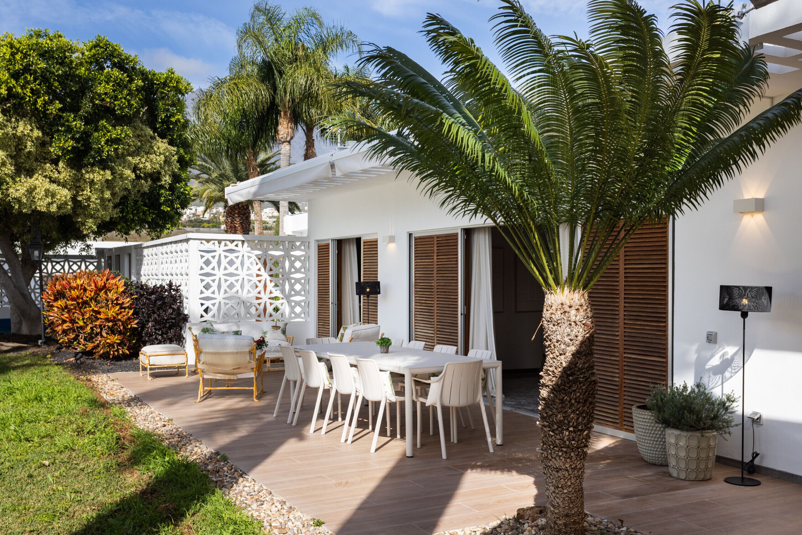 Een terras met een eettafel en stoelen, omringd door een witte hek en palmbomen.