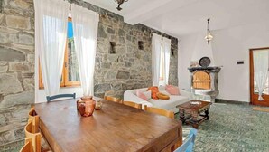 Ein Zimmer mit Steinwänden, einem Kamin, einem Holztisch und einer Couch mit Kissen.