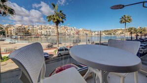A balcony with a table and chairs overlooking a marina with boats and a cityscape in the background. - Seafront home with private terrace in Marsascala (Marsaskala)