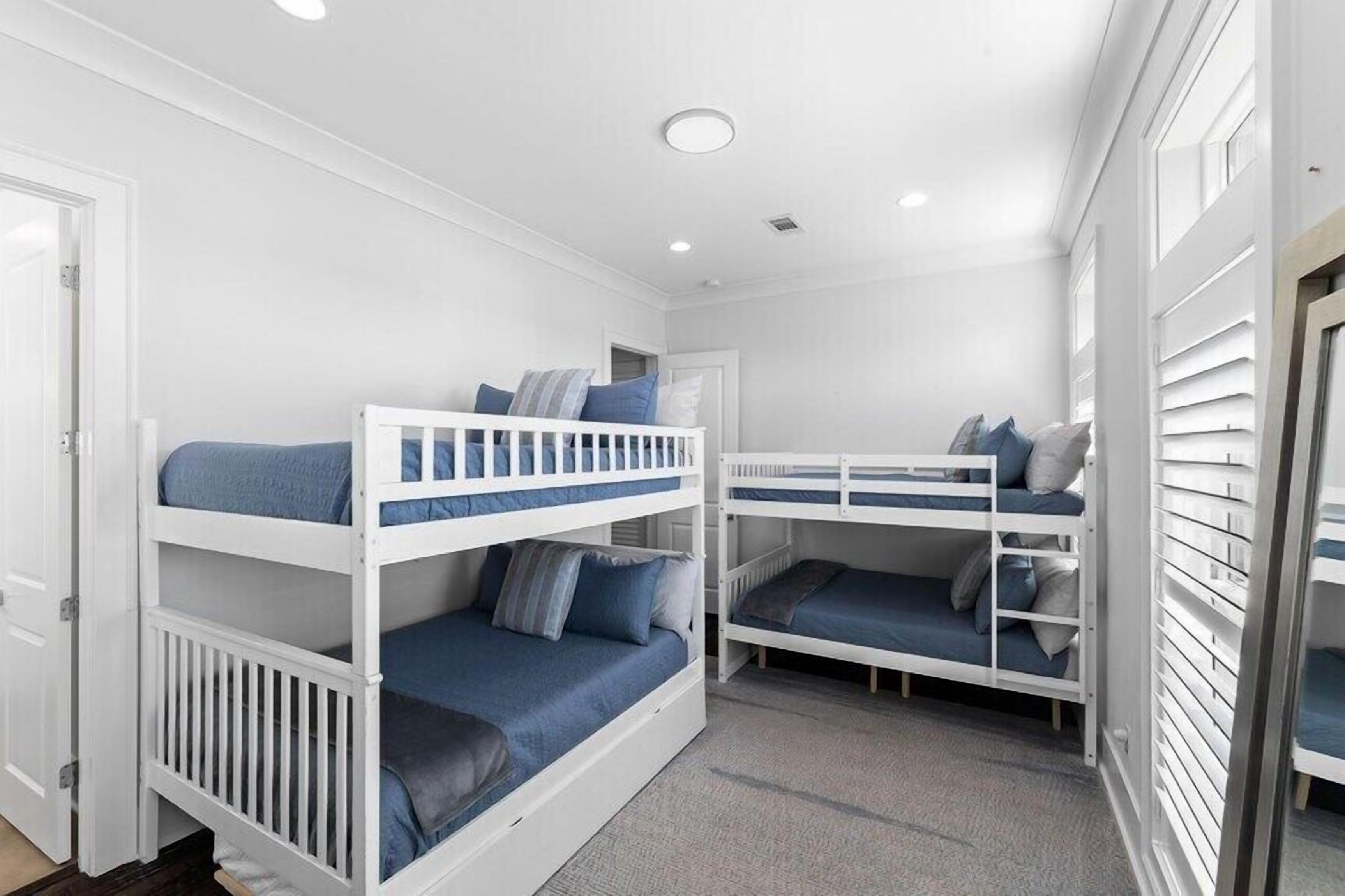 A room with two bunk beds, each with blue bedding and pillows, white railings, and a carpeted floor.