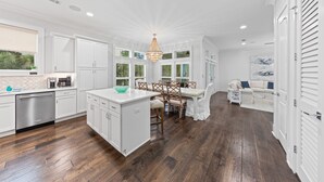Una cocina moderna con armarios blancos, una isla central y un comedor con candelabro.