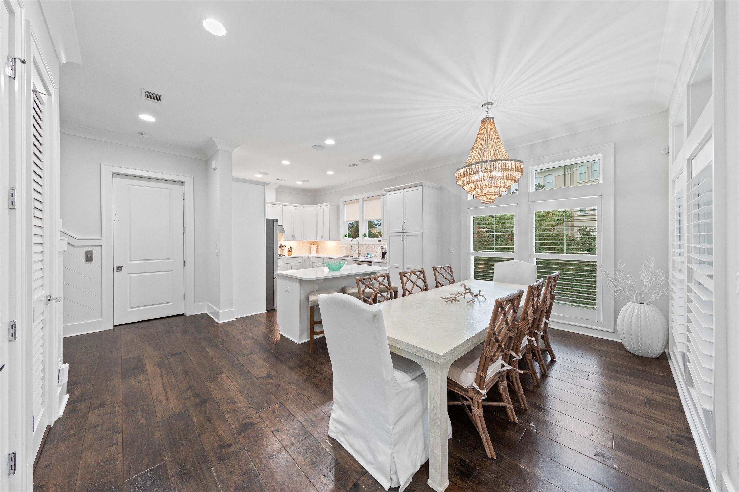 A spacious kitchen with white cabinetry, a central island, and a dining area with a white table and chairs.