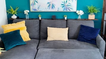Un canapé d’angle gris avec trois coussins, dans un salon aux murs de couleur turquoise.