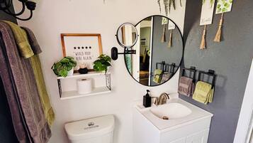 A modern bathroom with a toilet, sink, and mirror. There are plants on shelves and a towel rack with towels.