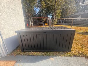 Ein schwarzer, freistehender Abstellschuppen mit Metallzaun, neben einer weißen Mauer und einem Rasen.