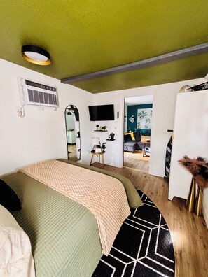 Une chambre à coucher comprenant un lit, une télévision, un miroir et une porte donnant sur une autre pièce.