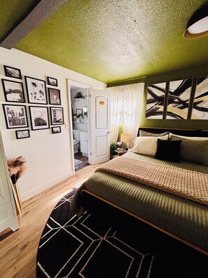 A bedroom with a bed, a nightstand, a lamp, and a wall with framed pictures.