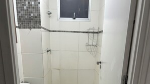 Een compacte, schone badkamer met toilet, douche en een raam.