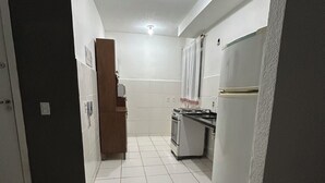 Een smalle gang die leidt naar een keuken met witte betegelde vloeren, een zwart tapijt en eenvoudige apparaten.