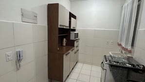 Een keuken met witte betegelde wanden, een houten kast, een magnetron, een gasfornuis en een telefoon.