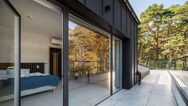 Une chambre moderne avec un grand lit, une porte vitrée donnant sur un balcon et une vue sur les arbres.