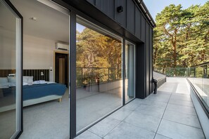 Ein modernes Schlafzimmer mit einem großen Bett, einer Glastür, die auf einen Balkon führt, und Blick auf Bäume.