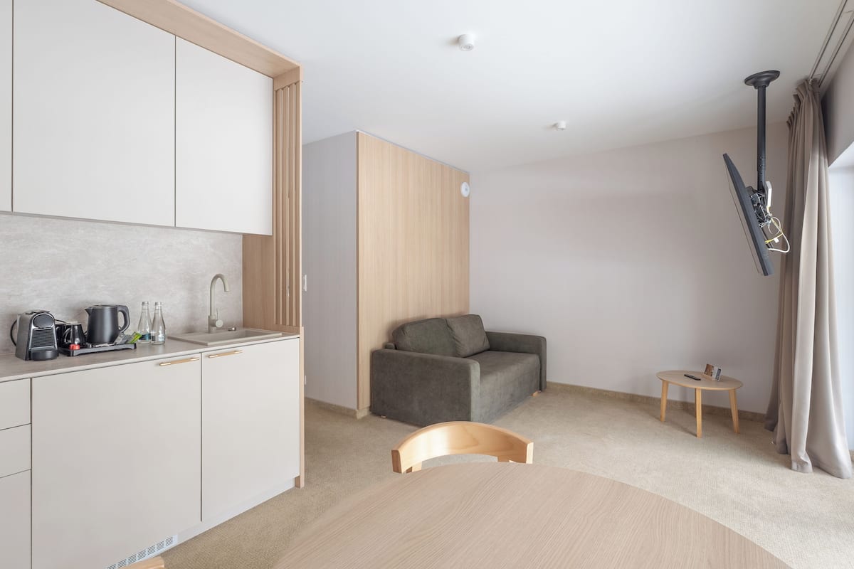 A modern kitchen with white cabinets, a grey sofa, a small round table, and a wooden chair.