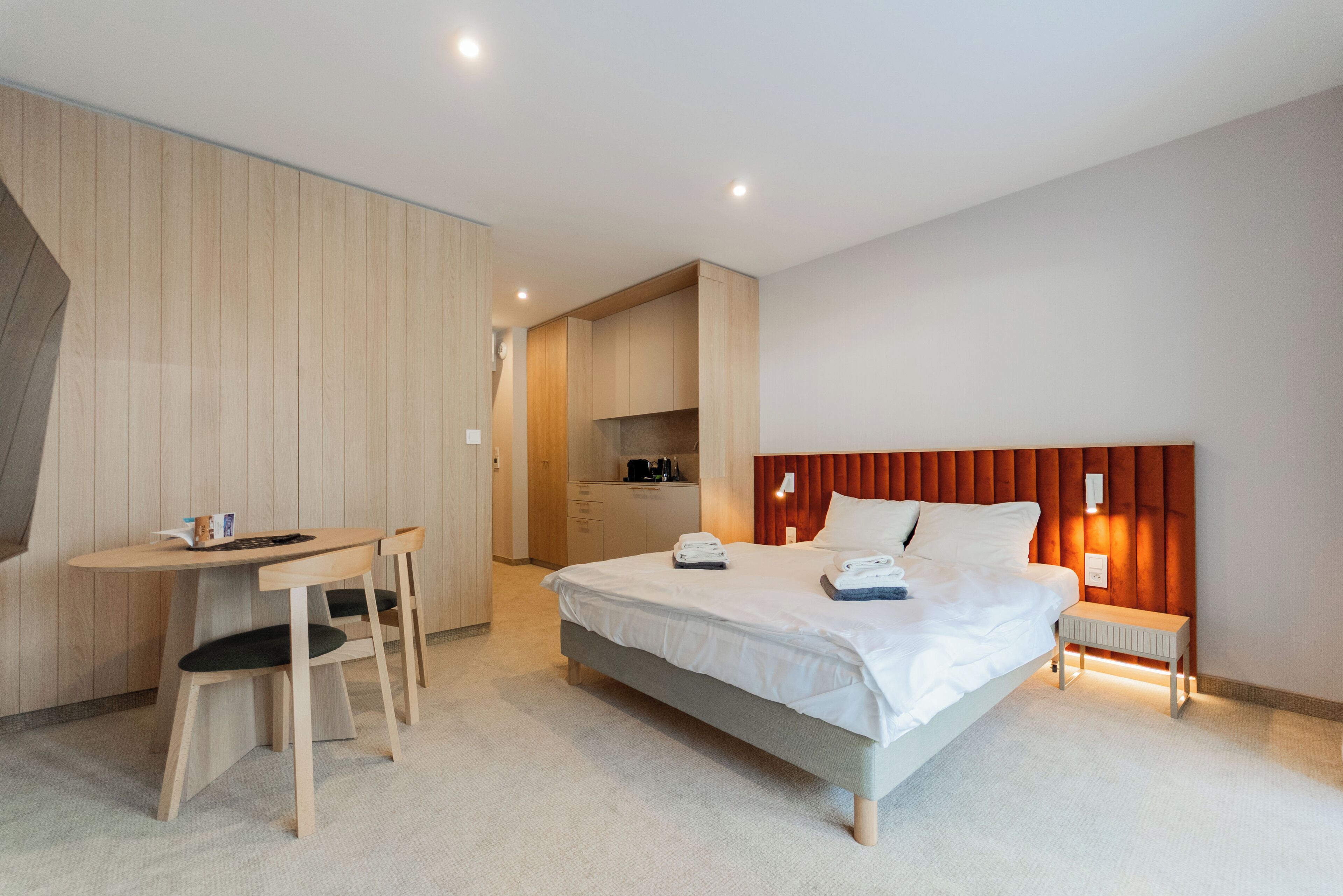 A modern hotel room with a bed, a desk, and a kitchenette.