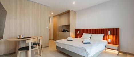 A modern hotel room with a bed, a desk, and a kitchenette.