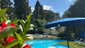 Ein Schwimmbad mit Liegestühlen und Sonnenschirmen, umgeben von viel Grün.