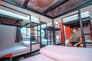 A hostel room with bunk beds, a window with curtains, and a view of buildings outside. - Brick House Hostel Chiangmai (Chiang Mai)