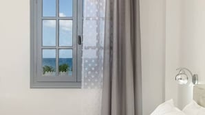A bedroom with a window overlooking the sea, a bed, and a bedside lamp. - Sea & Sky Luxury Beach House – Elegant Cycladic Studio by Agia Paraskevi Beach (Kamari)
