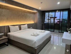 A modern hotel room with a large bed, bedside tables, a small desk, and a balcony with a view. - Raw Hostel (Chiang Mai)