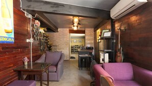 A cozy room with a wooden wall, a purple sofa, a small table, and a ceiling fan. - Raw Hostel (Chiang Mai)