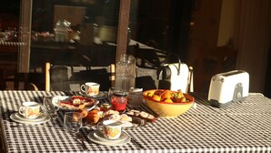 Une table à carreaux avec des aliments pour le petit-déjeuner, notamment des viennoiseries, un saladier de fruits et une théière.