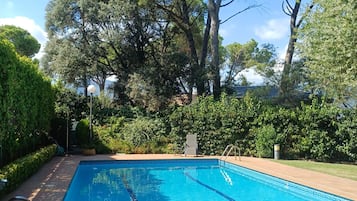 Una piscina rectangular con agua azul cristalina, rodeada por un solárium con baldosas y abundante vegetación.