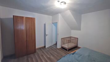 A room with a wooden wardrobe, a crib, and a bed.