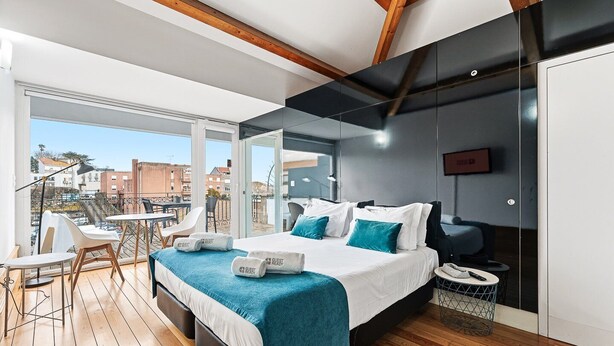 A modern hotel room with a large bed, a balcony with outdoor seating, and a city view.