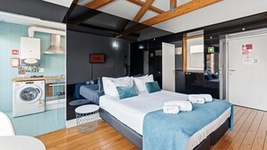A modern hotel room with a large bed, a washing machine, and a compact kitchenette.